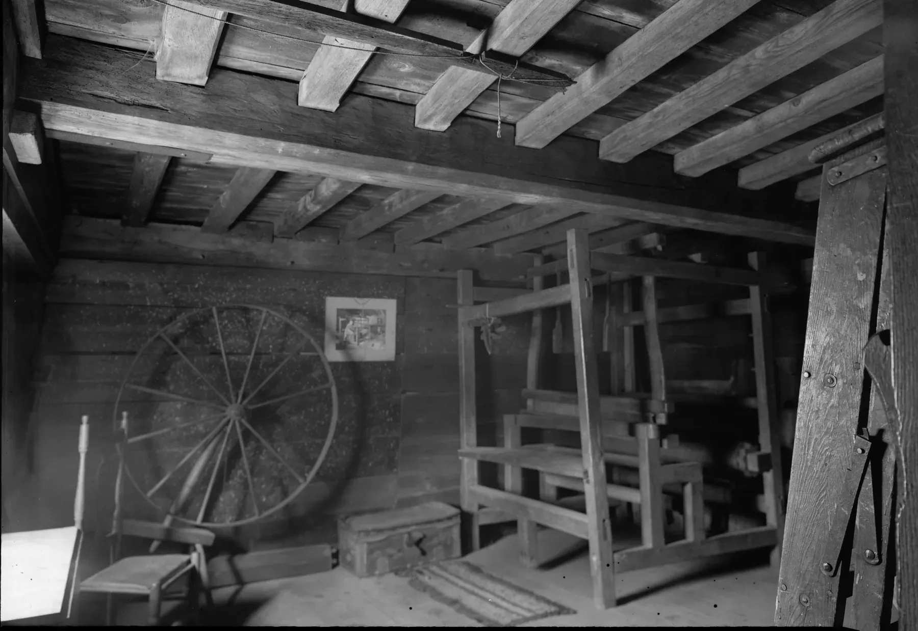 Cuarto de trabajo del piso alto de la casa Fairbanks con vigas labradas a mano a la vista, un telar, una rueca y piso de tablones