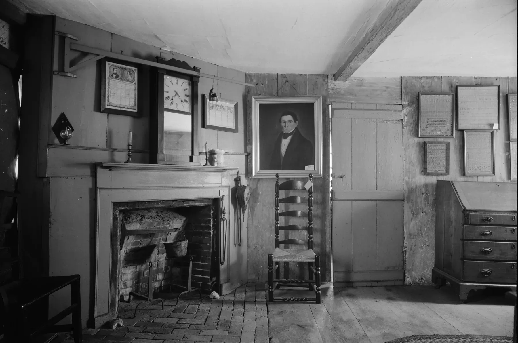Sala de la casa Fairbanks con hogar de ladrillo, una silla de respaldo de escalera, un escritorio de tapa inclinada y piso de tablones anchos