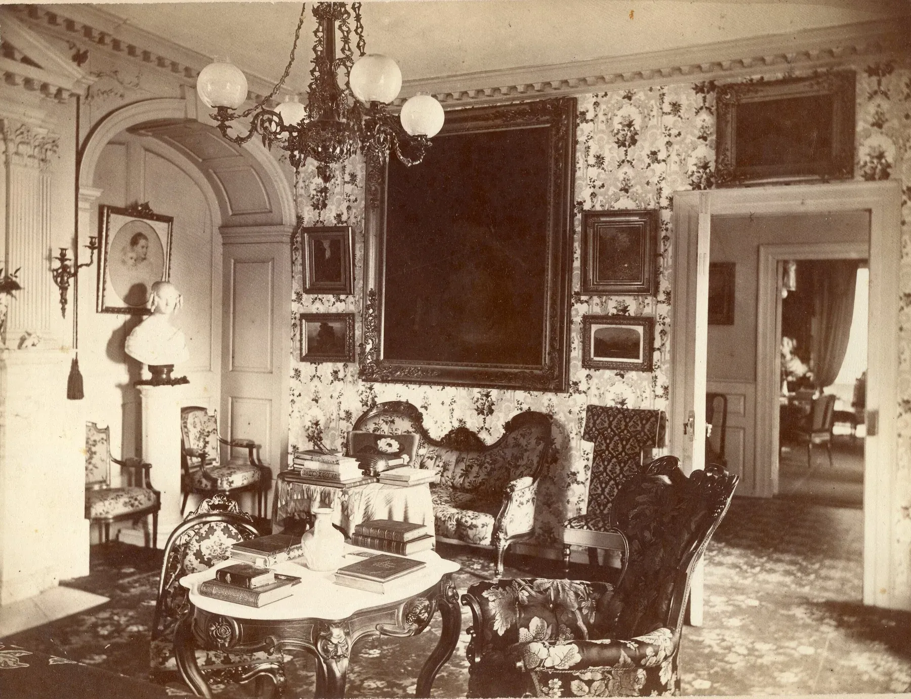 Fotografía de 1871 de la sala de la casa Longfellow con papel tapiz de flores, una lámpara de gas, sillas tapizadas y una alfombra con diseño que cubre todo el piso