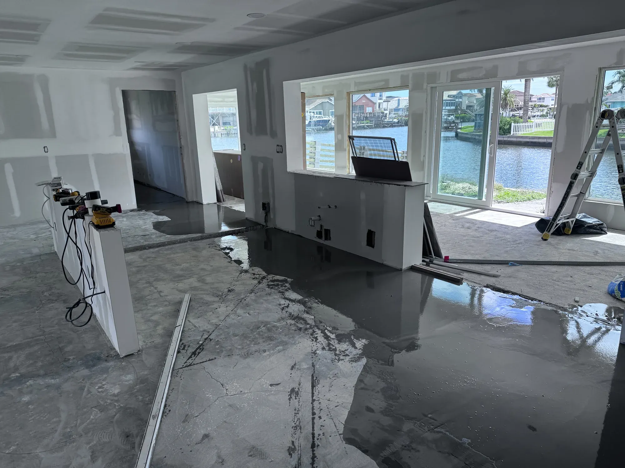 Waterfront living area under construction, with bare drywall and a concrete slab patched with leveling compound