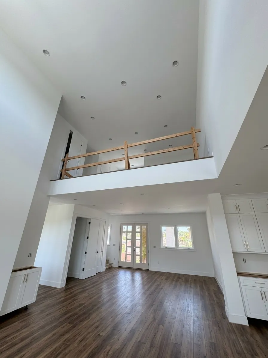 The same double-height great room finished, with dark oak-look laminate running from the kitchen cabinetry to the front doors