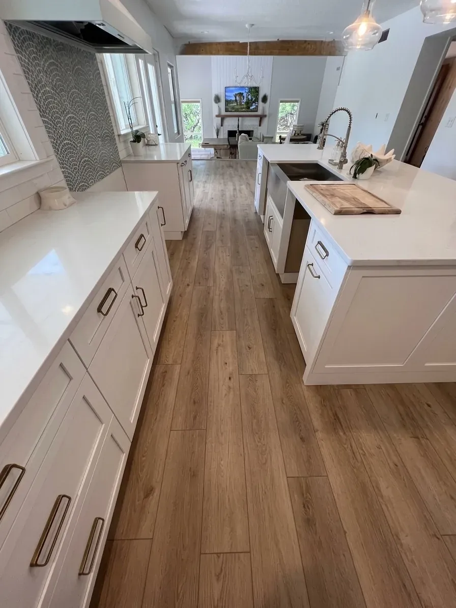 The same kitchen with warm oak-look vinyl plank installed, running between the white cabinets and the island
