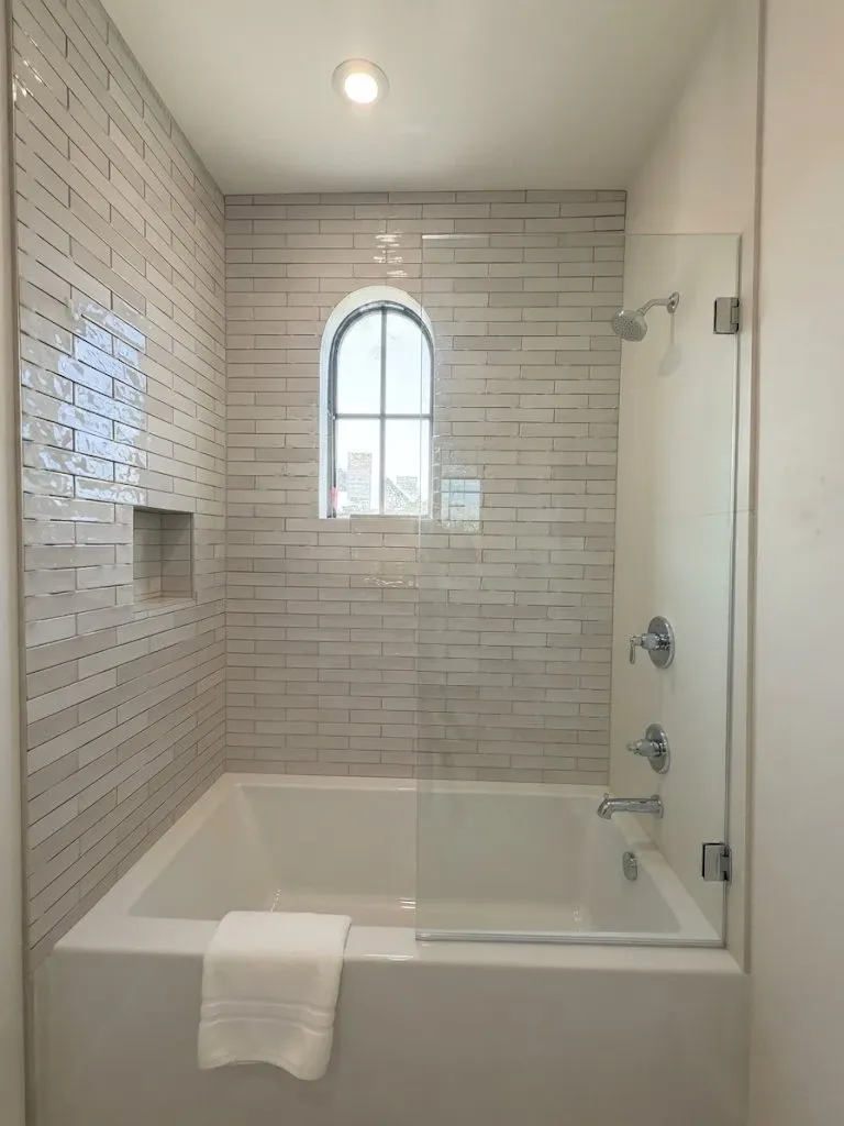 The same bathroom finished, with the tiled tub surround, a recessed niche and a glass splash panel