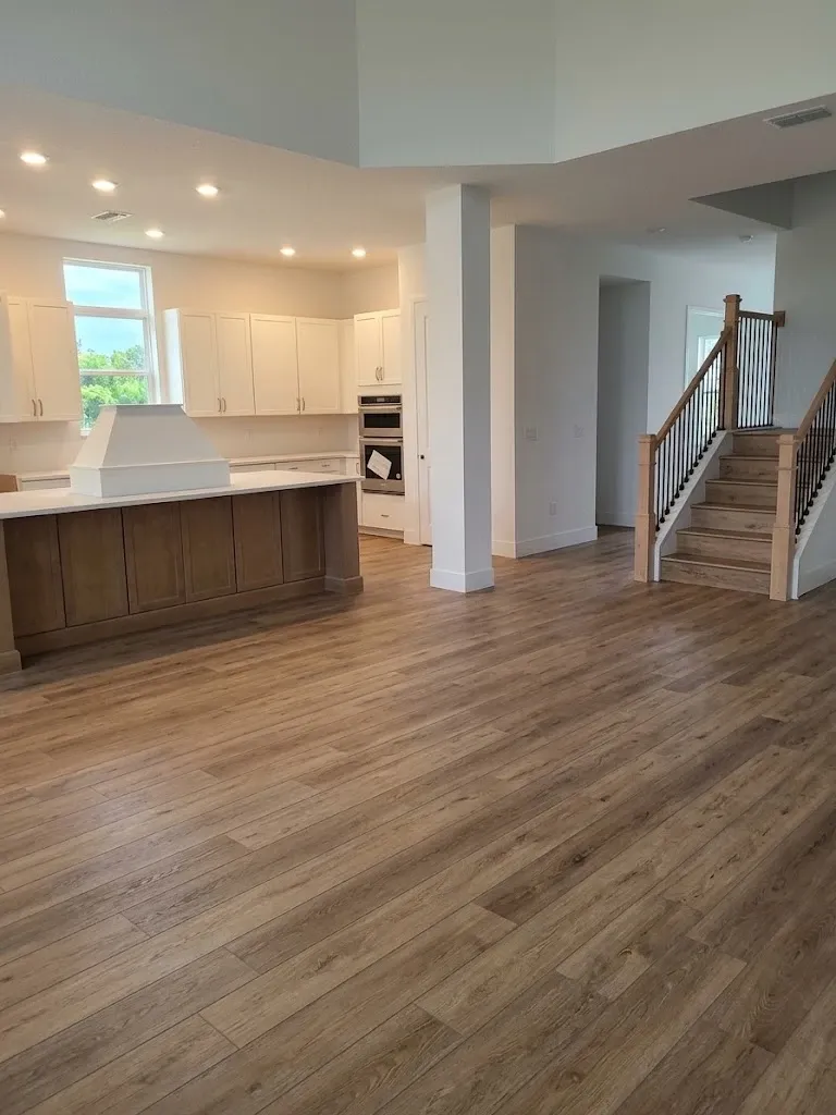 The same kitchen and living area finished, with warm oak-look vinyl plank running from the island across to the staircase