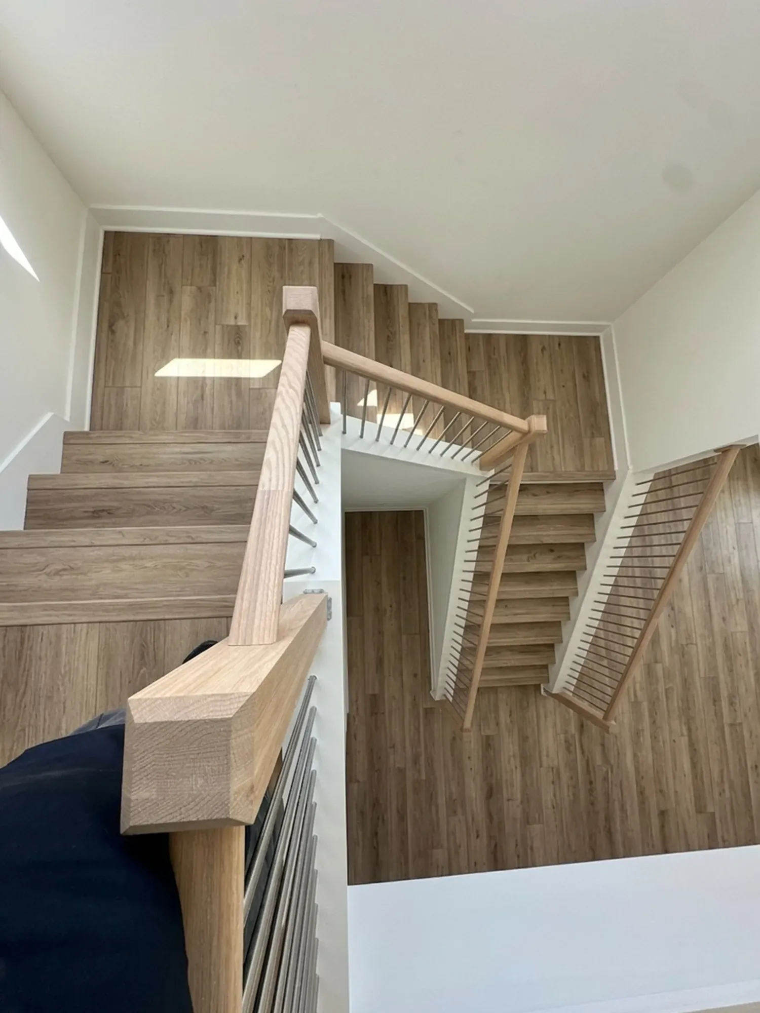 The same staircase with oak-look vinyl plank on treads, risers and landing, seen from the same top step