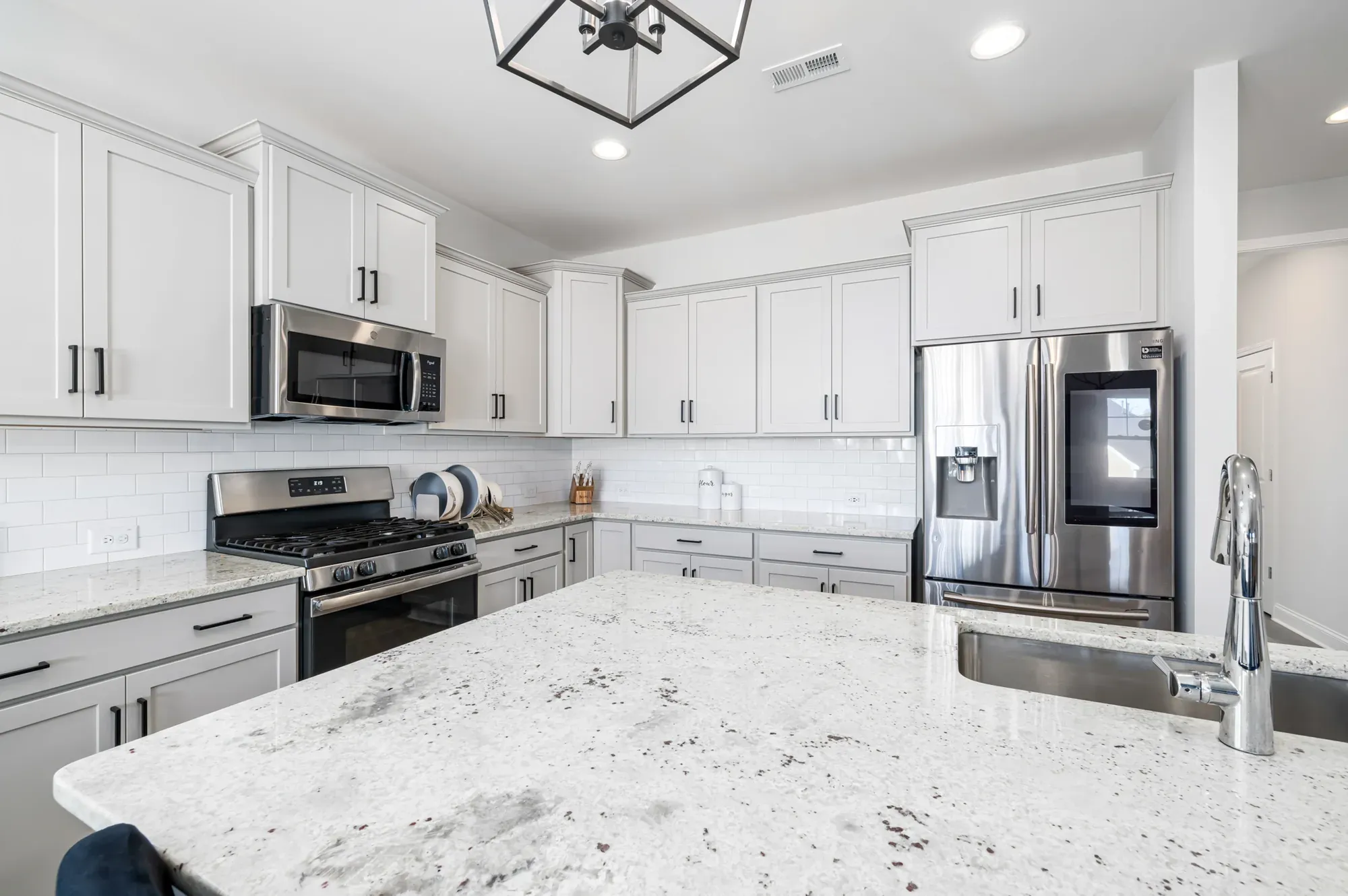 A white kitchen with shaker cabinets, a subway tile backsplash and a light veined countertop running along the counter and over the island