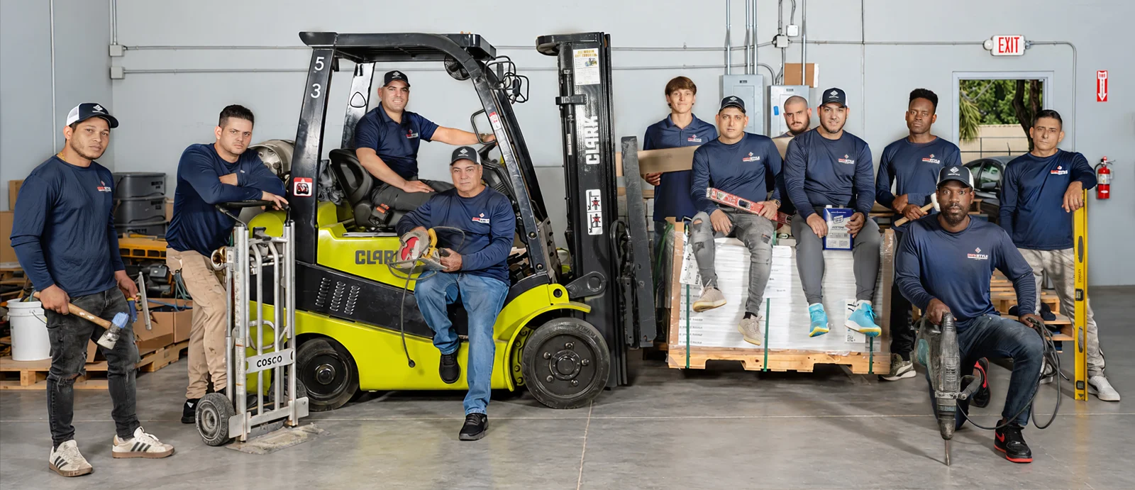 The Flooring at Tampa Bay team with its installation crews in the warehouse, gathered around a forklift and pallets of flooring
